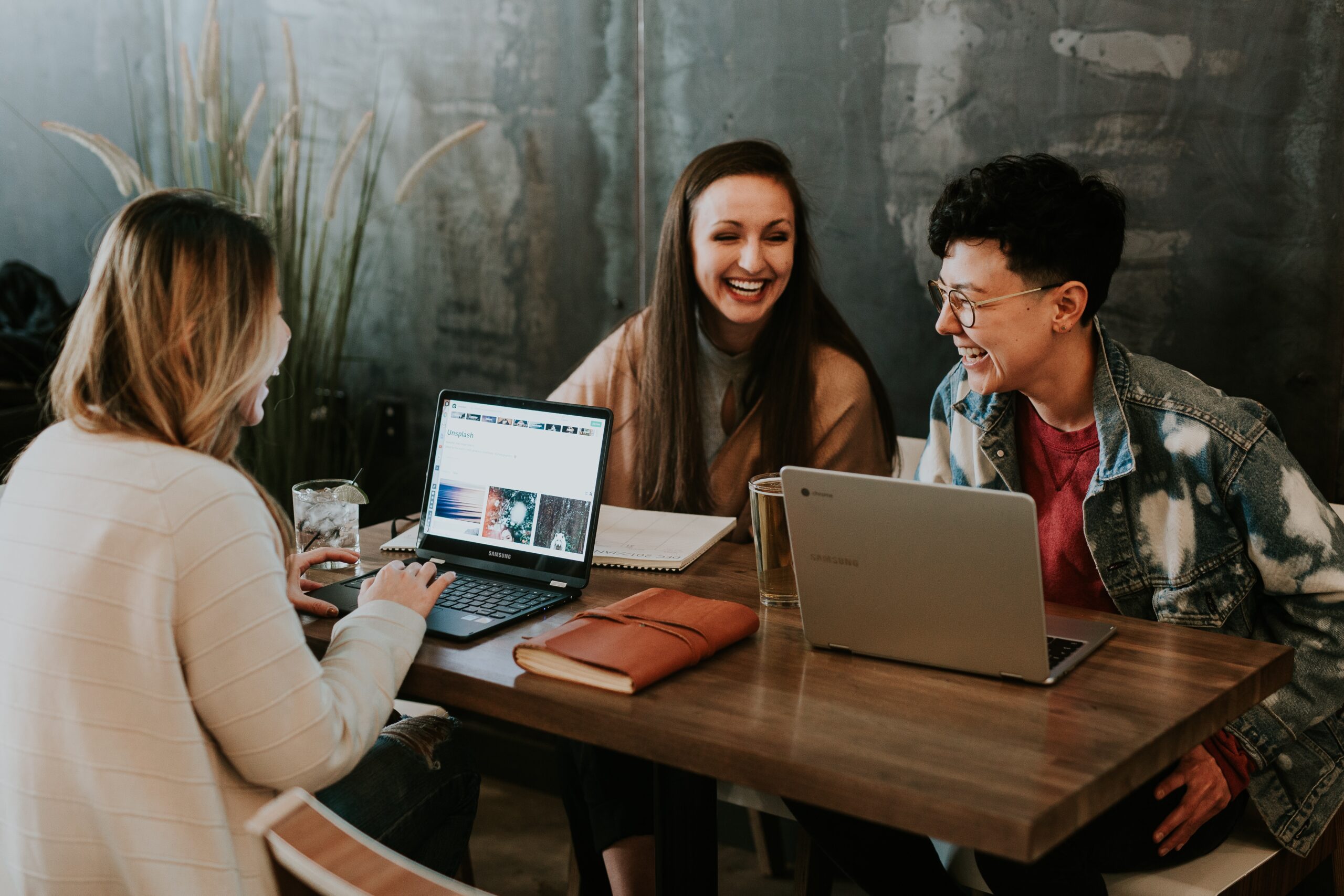 Three gender diverse colleagues at work sit around a table talking.