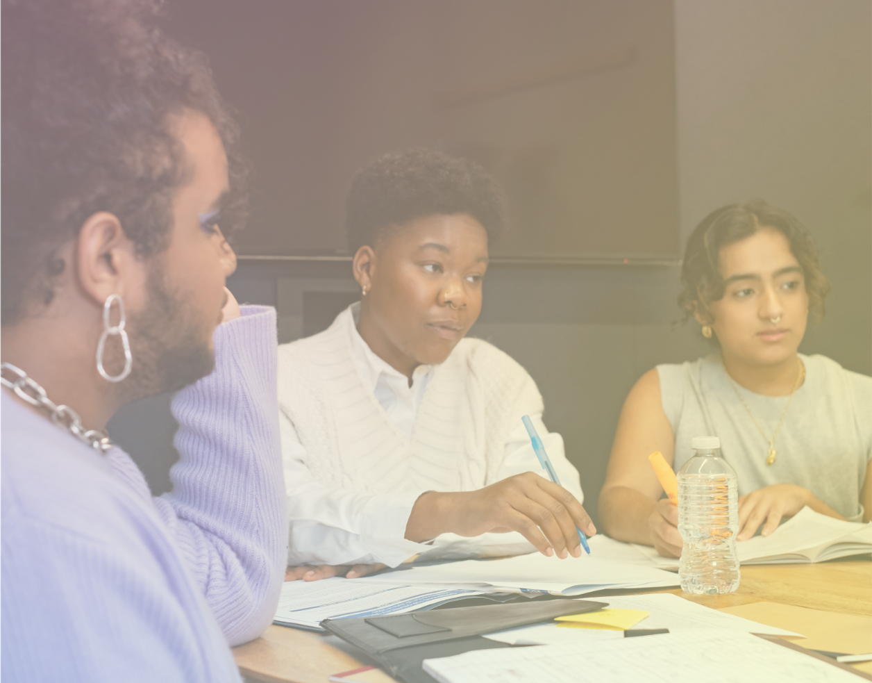 Three people sit around a table in a classroom.