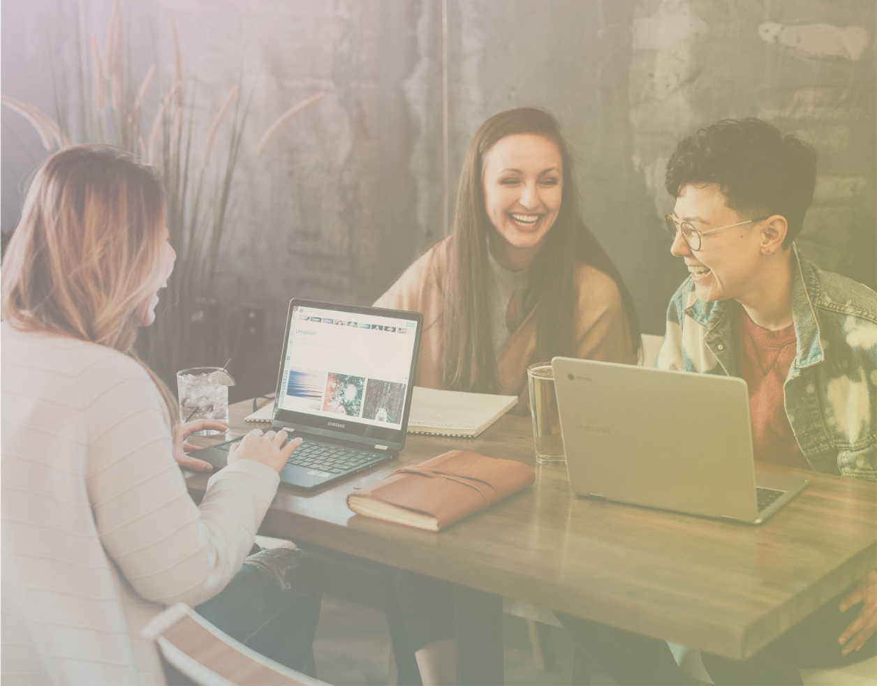 Three employees of diverse gender expressions laughing around a table